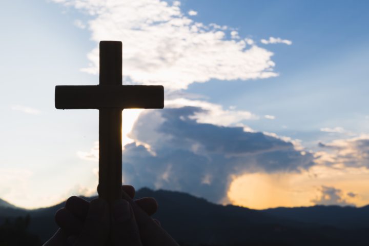cropped-hand-holding-religious-cross-against-sky